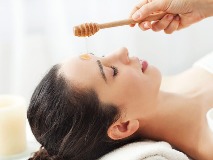 Woman waits patiently as a hand pours honey onto her face for a face mask